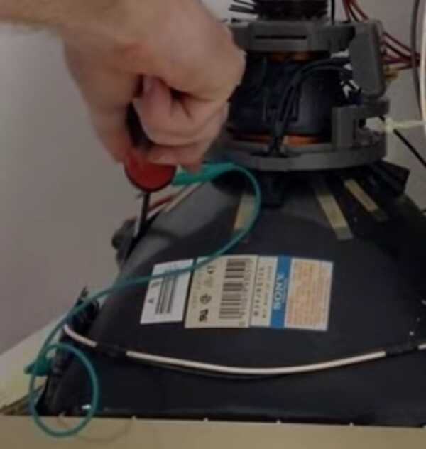 A hand holding a screwdriver with an alligator clip attaching the screwdriver to the case chassis. The tip of thhe screwdriver is inserted into the suction cup covering the anode wire of the CRT.